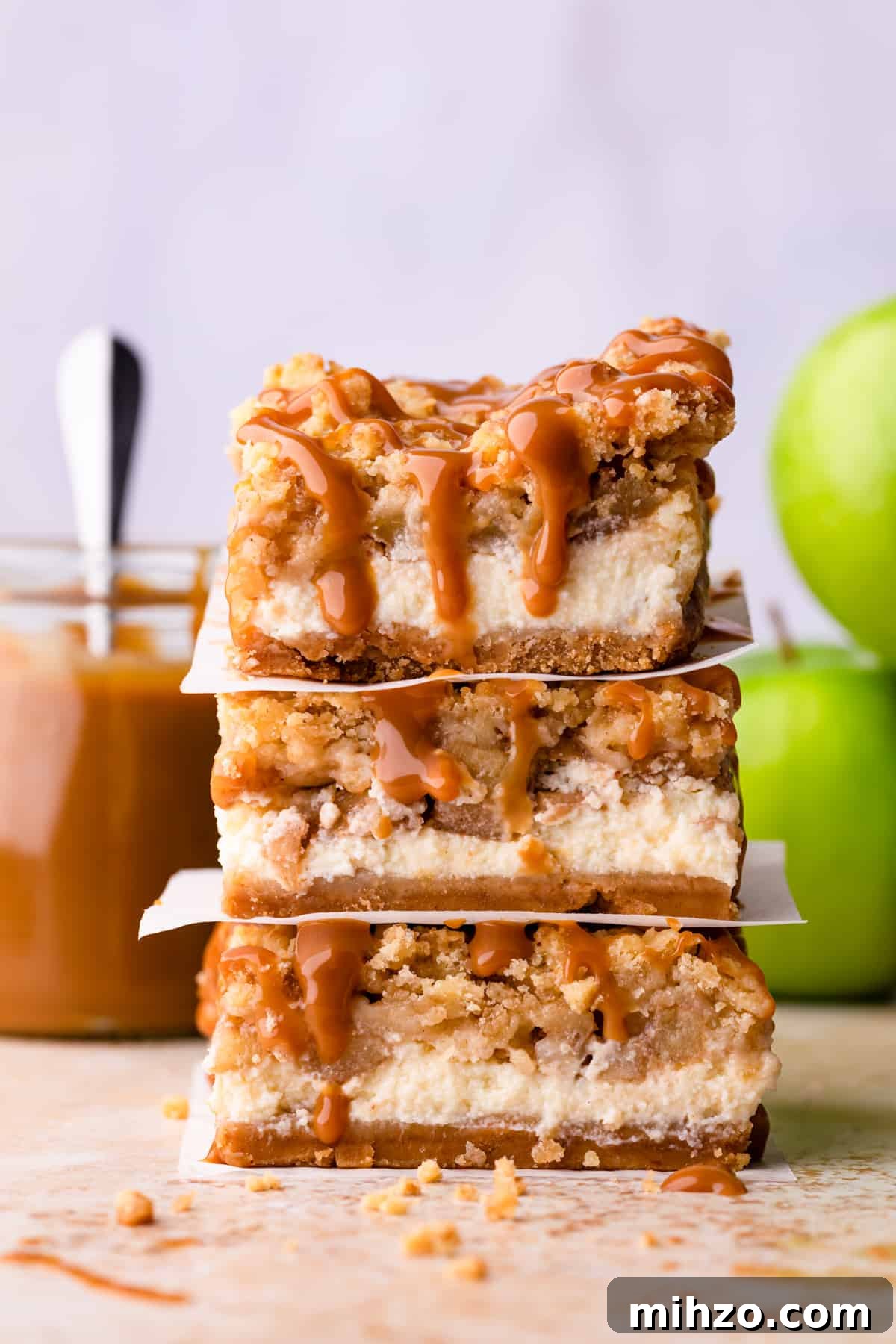 stack of three caramel apple cheesecake bars with caramel dripping from them.