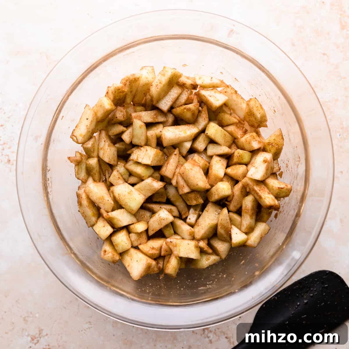 mixing bowl with chopped apples covered in spices.