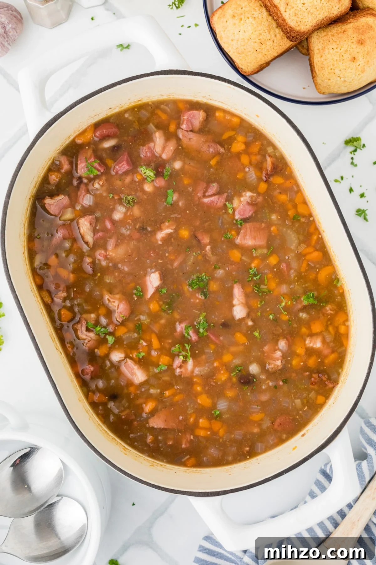 A pot full of bean and ham soup on a white tile background.