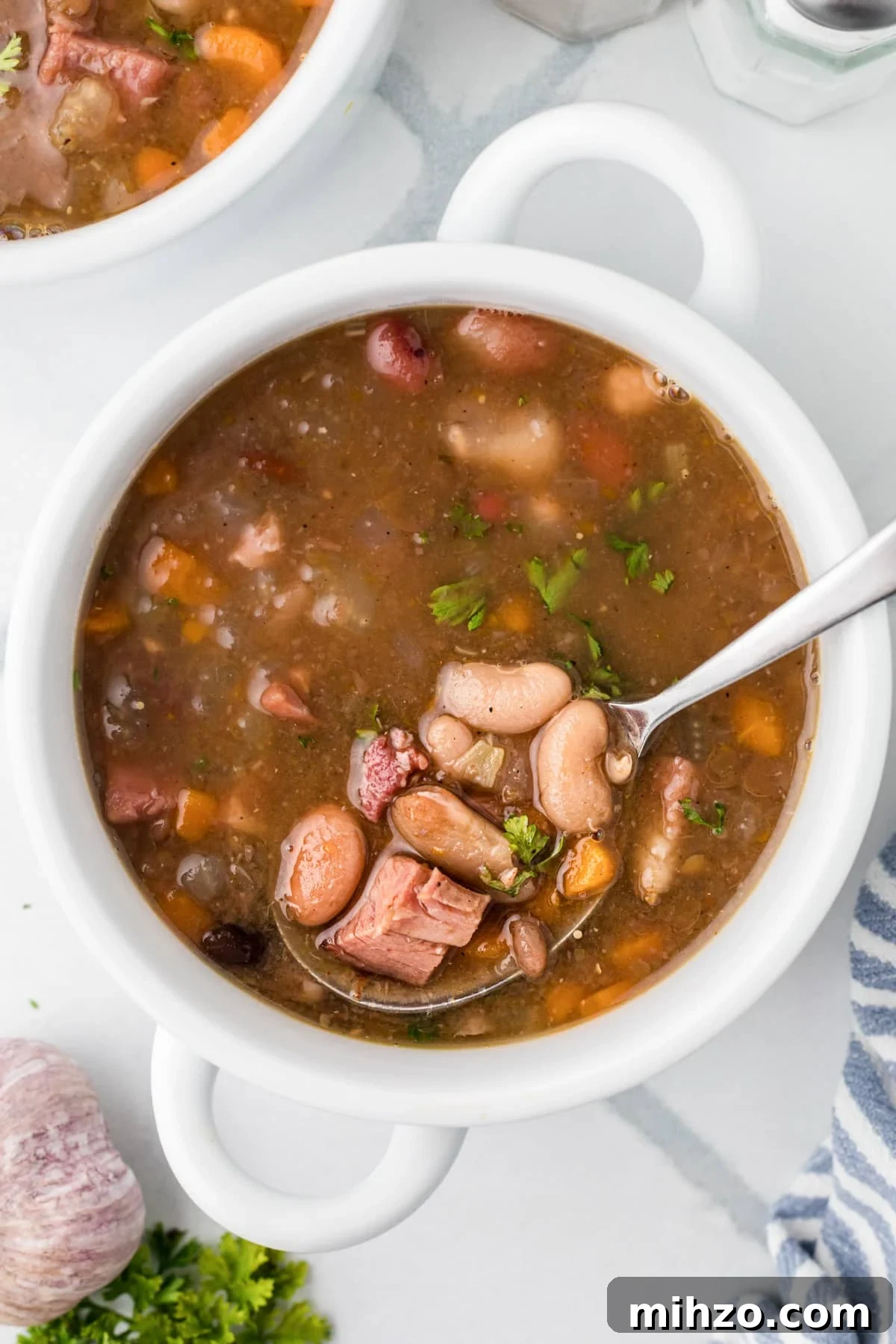 A spoon in a bowl of soup, with small bits of beans and ham floating around.