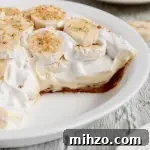 A vegan banana cream pie topped with bright white fluffy whipped topping and banana slices.