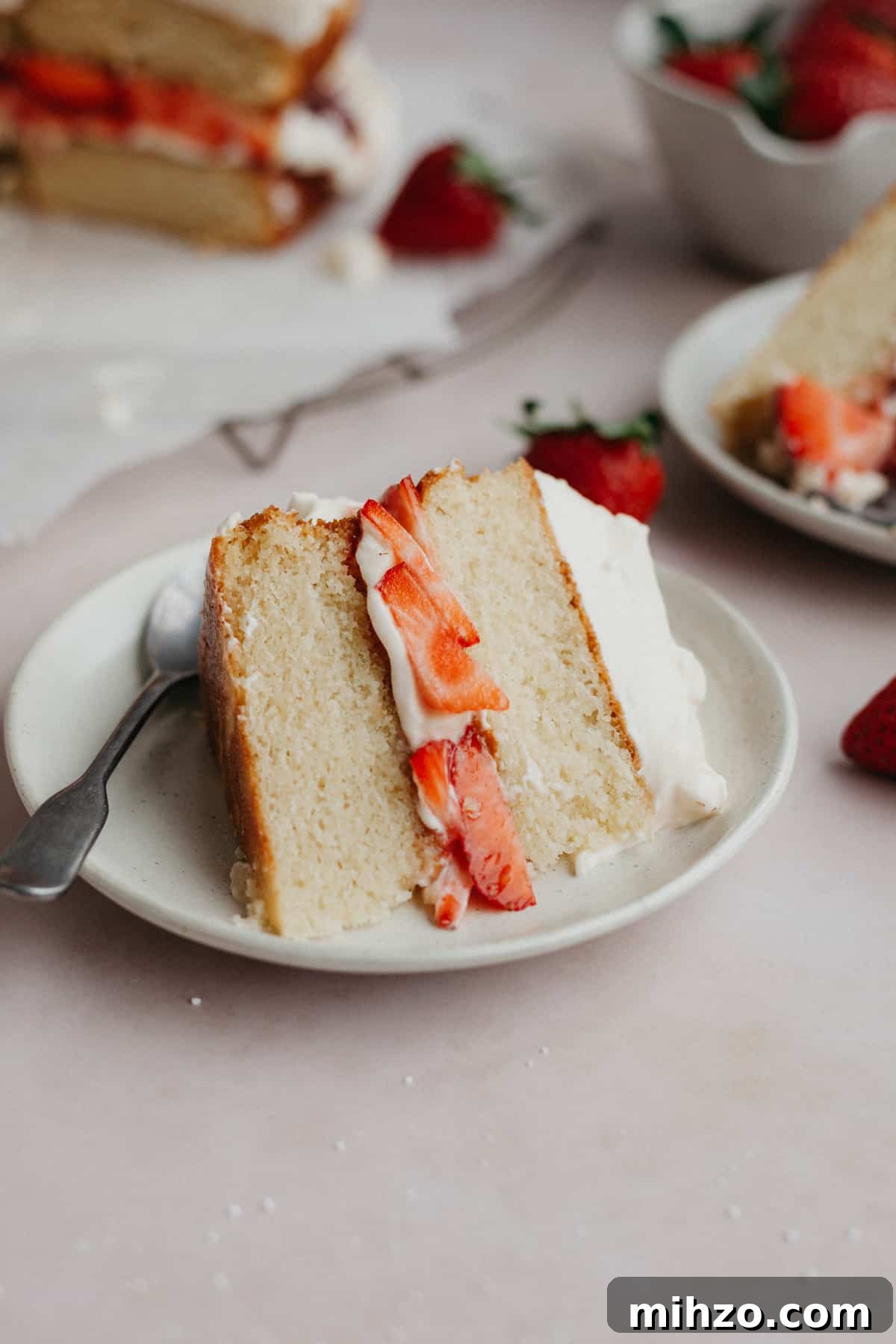A slice of white cake that has a strawberry filling, on a small beige plate