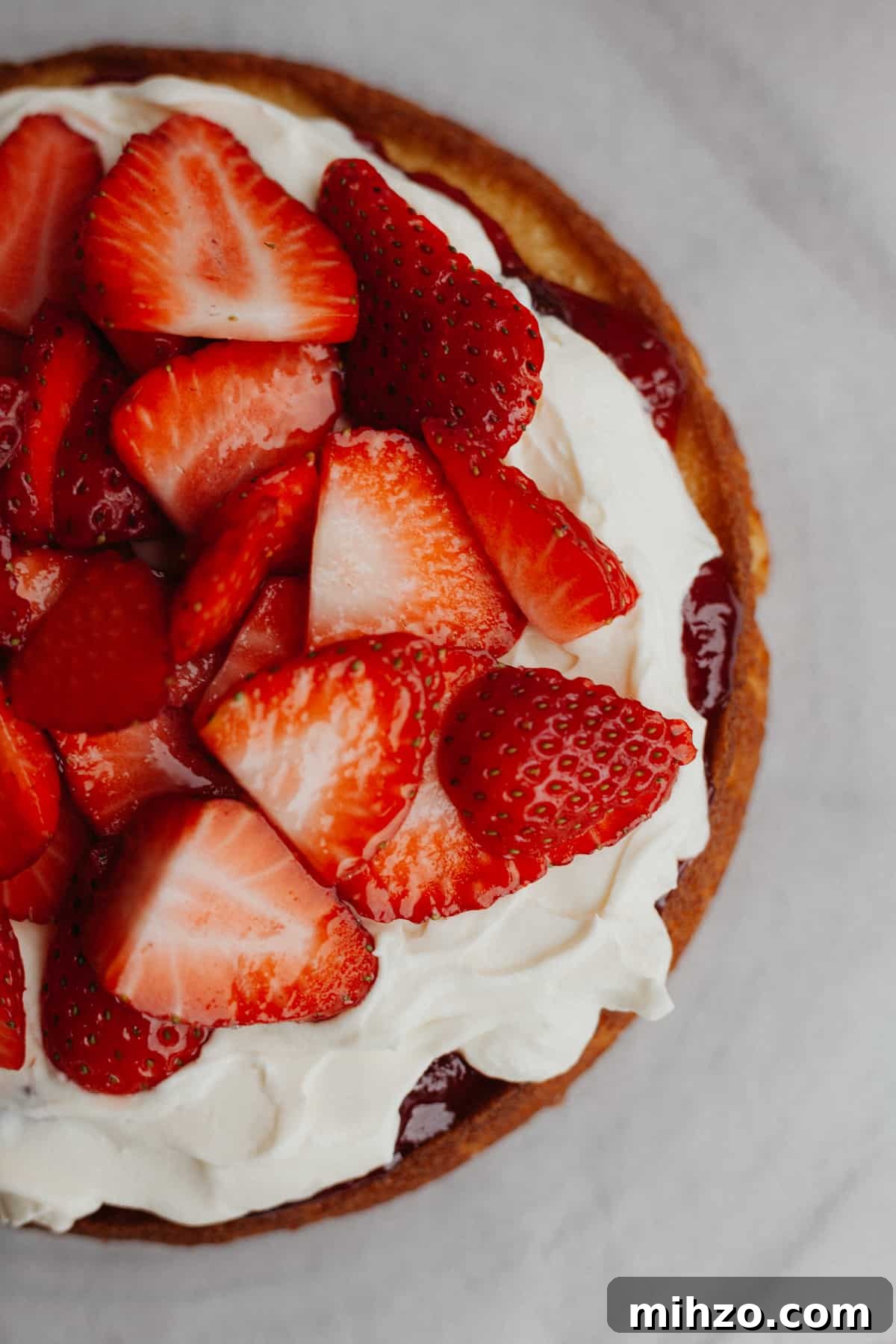An overhead shot of a strawberry filled cake. You see the bottom cake layer, jam, whipped cream, and then strawberries.