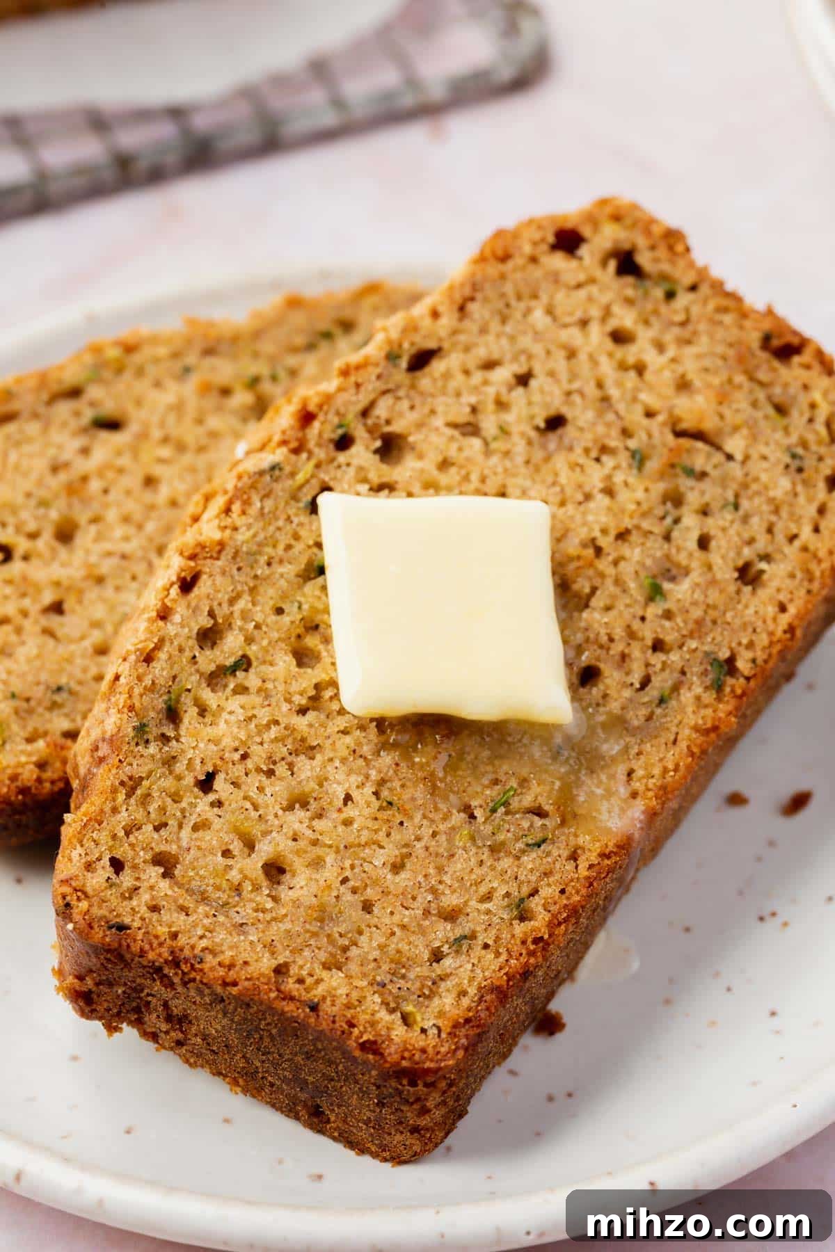 Moist Gluten-Free Zucchini Bread Recipe for Baking Success 4 Two slices of gluten-free zucchini bread stacked on a small plate with a slice of melting butter on top.