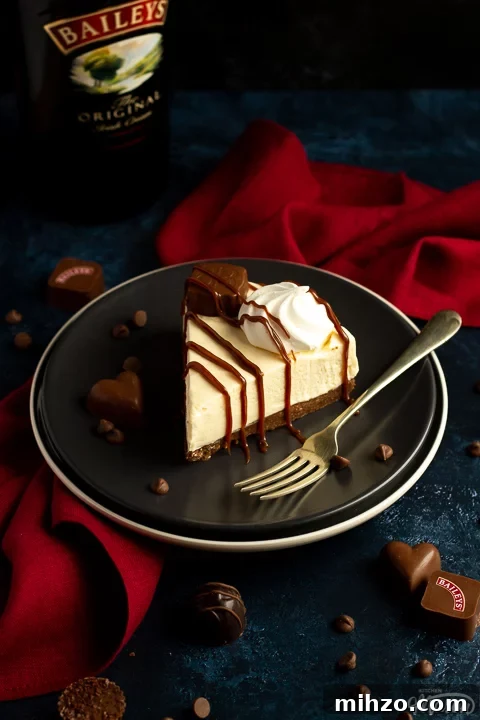 No-Bake Baileys Cheesecake Recipe: Creamy Irish Cream Dessert 8 A slice of no bake Baileys cheesecake on a dark grey plate with a fork and Baileys in background