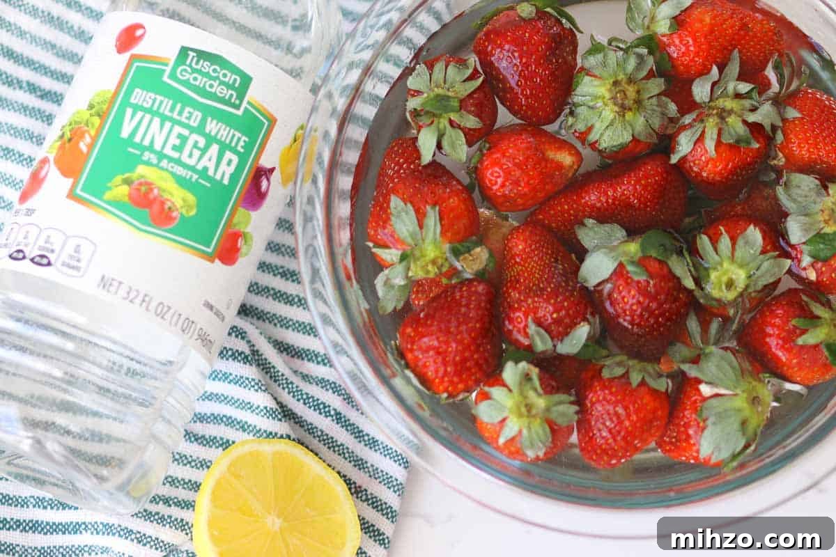 Wash Fruit with Vinegar: DIY Produce Cleaning Spray 6 a bottle of vinegar laying next to a lemon and a bowl of strawberries soaking in water