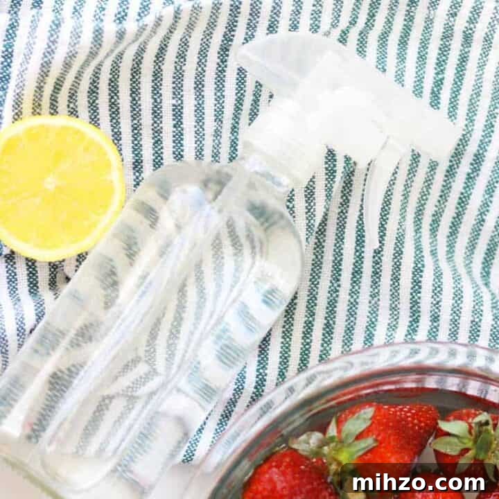 a glass spray bottle on a striped towel and a bowl of strawberries in a bowl of water and vinegar