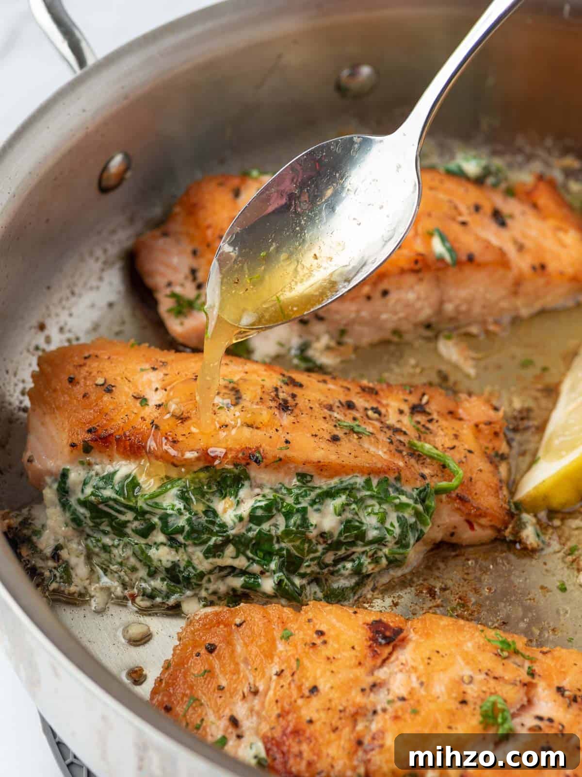 Creamy Spinach-Stuffed Salmon Fillets with Garlic Butter 8 A pan of creamy stuffed spinach salmon with sauce spooned on top.