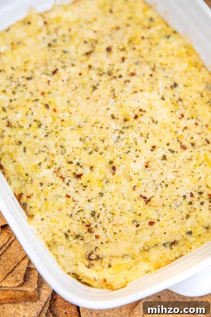baking dish of artichoke dip surrounded by wheat thins on a table