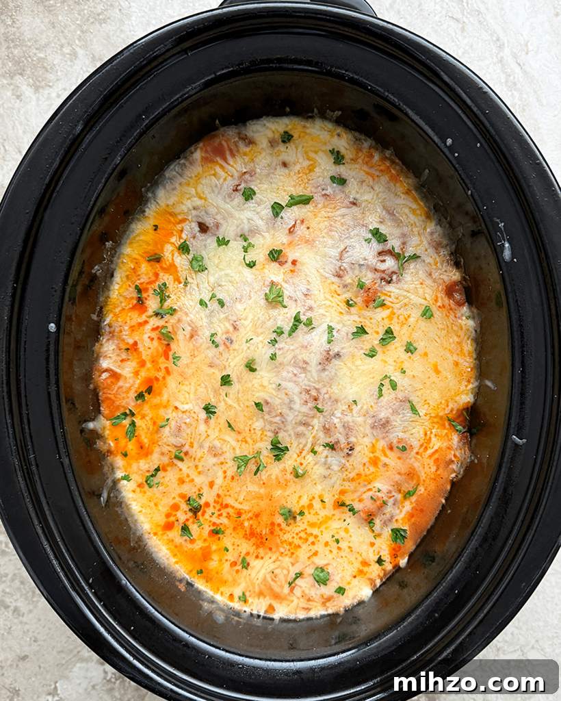 overhead shot of cooked ravioli casserole in a black slow cooker with melted cheese on top