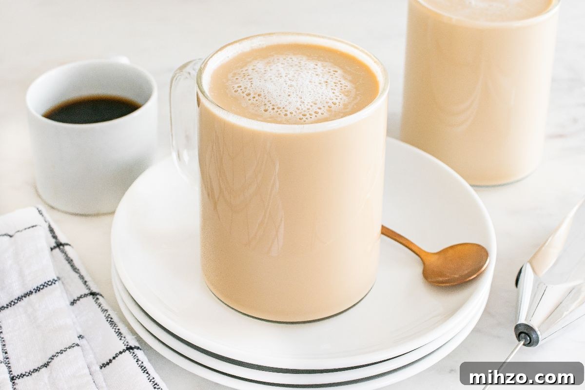 A mug of frothy latte breve on stacked plates with a spoon, next to a cup of black coffee and a napkin.