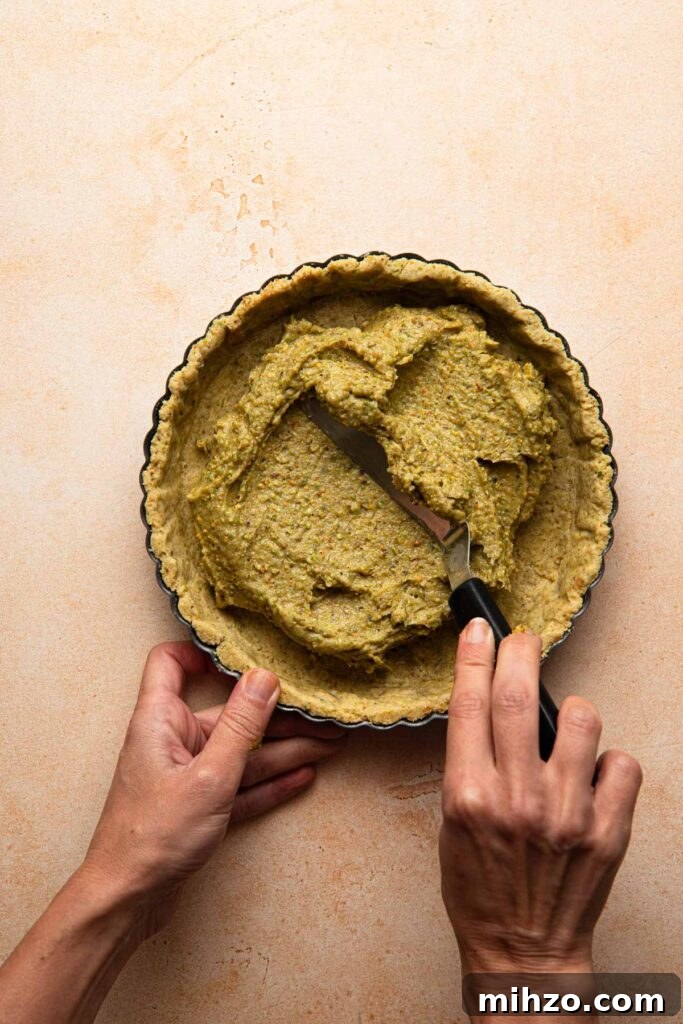 Pistachio Frangipane Tart Recipe — Crunchy Almond-Pistachio Filling 5 A hand spreading pistachio cream into a tart shell.