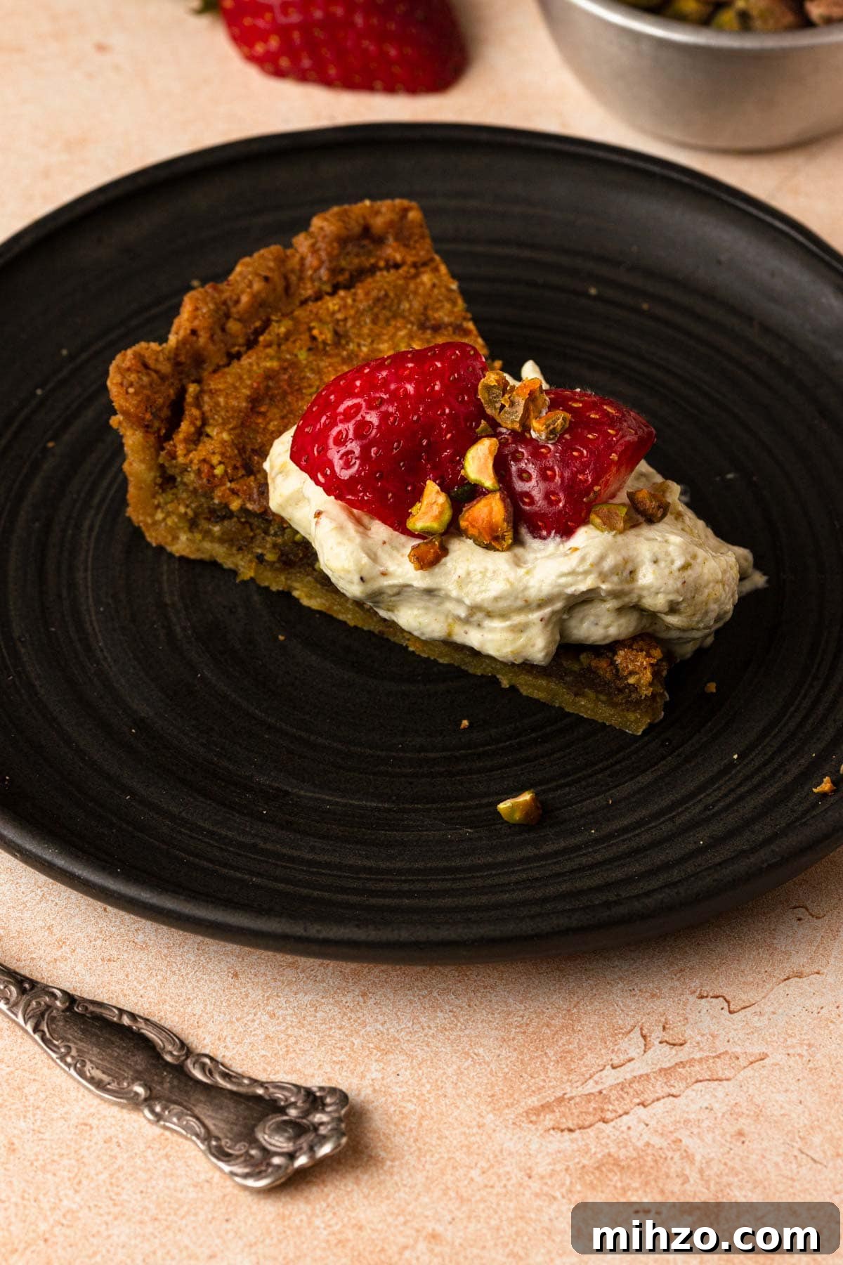 Pistachio Frangipane Tart Recipe — Crunchy Almond-Pistachio Filling 8 A piece of pistachio tart topped with whipped cream and fresh strawberries.