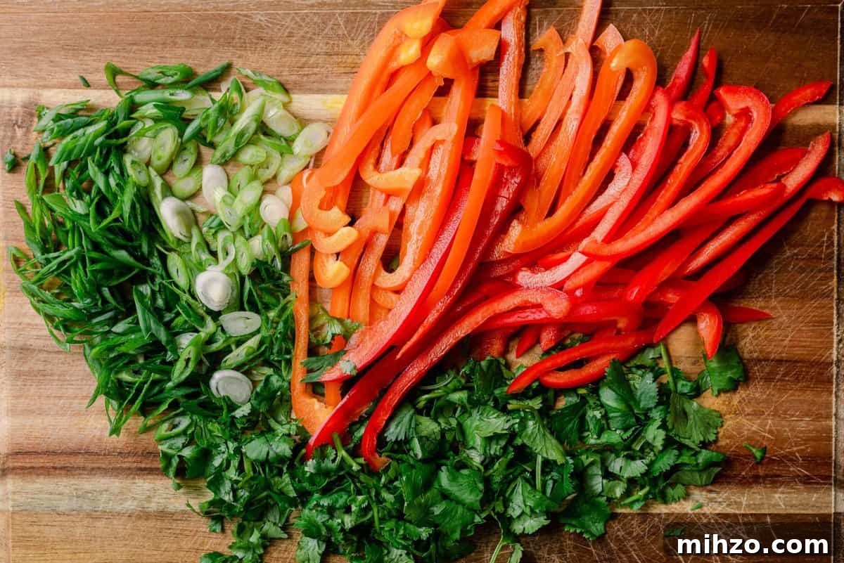red and orange bell pepper slices on cutting board with sliced scallions and cilantro