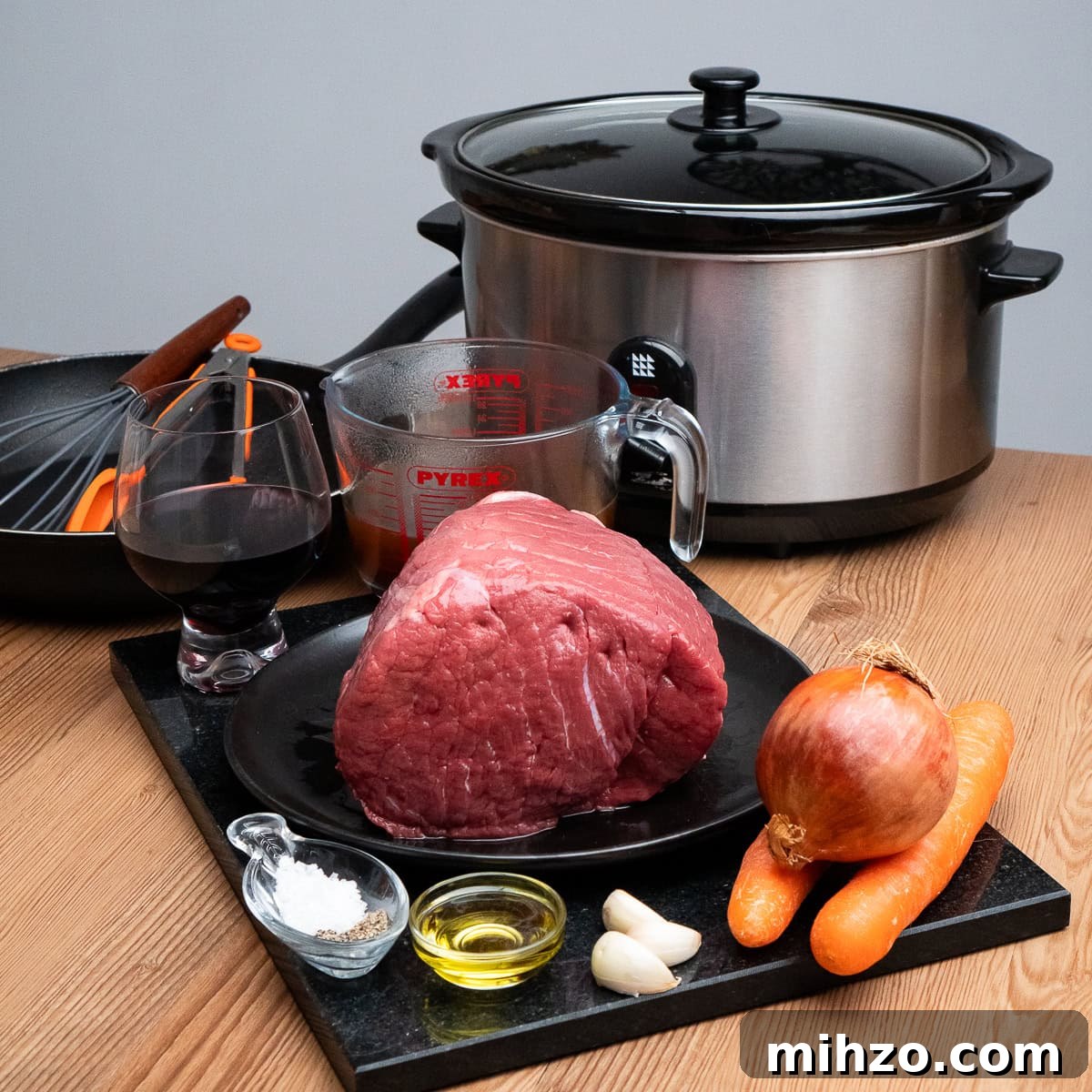 A raw beef joint,slow cooker,one onion,two carrots three garlic cloves,olive oil,red wine in a glass,beef stock in a jug,a frying pan,whisk and tongs