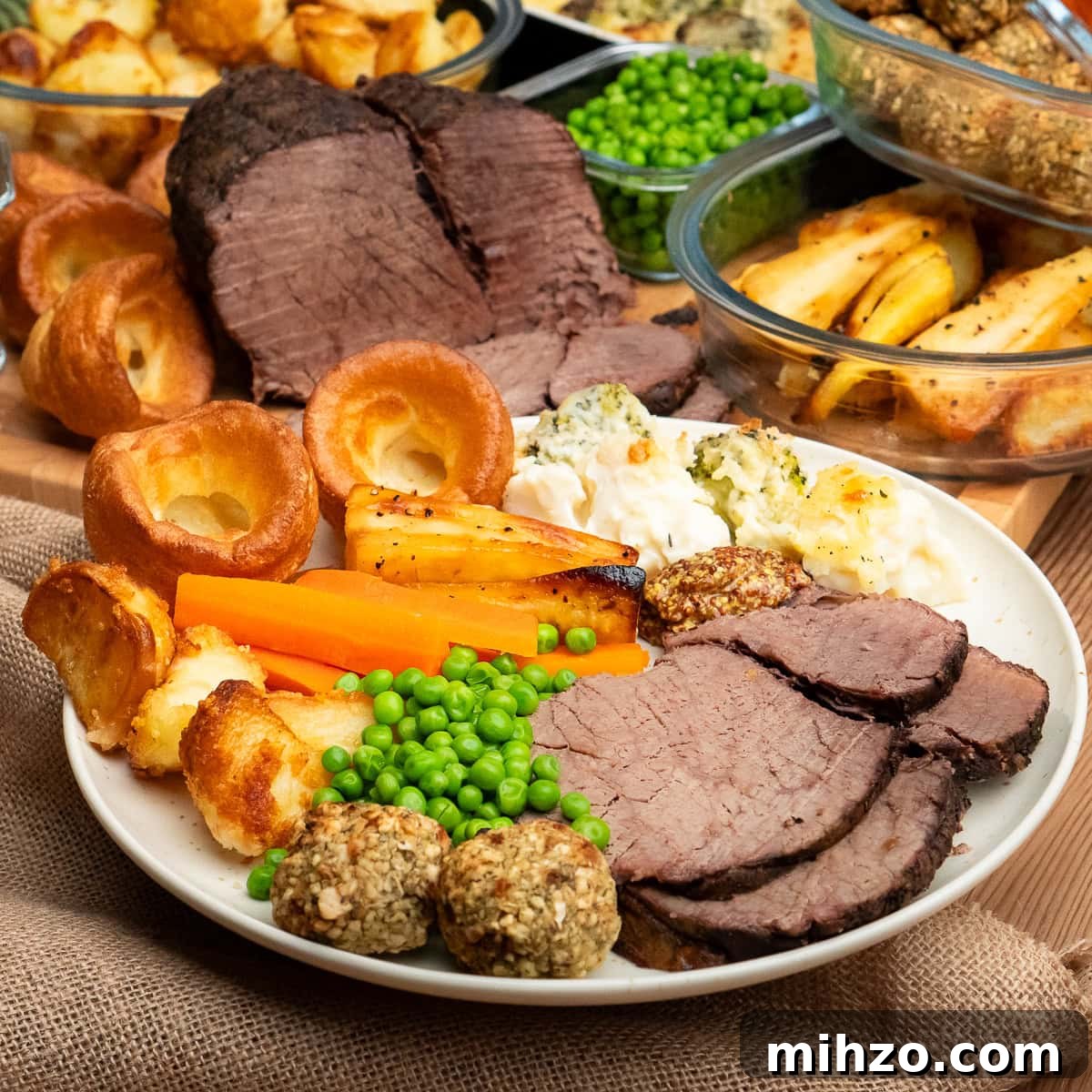 Slow cooker roast beef sliced on a plate served with roast dinner trimmings like cauliflower and broccoli cheese,Yorkshire puddings,parsnips, peas ,roast potatoes,carrots, stuffing balls and whole grain mustard