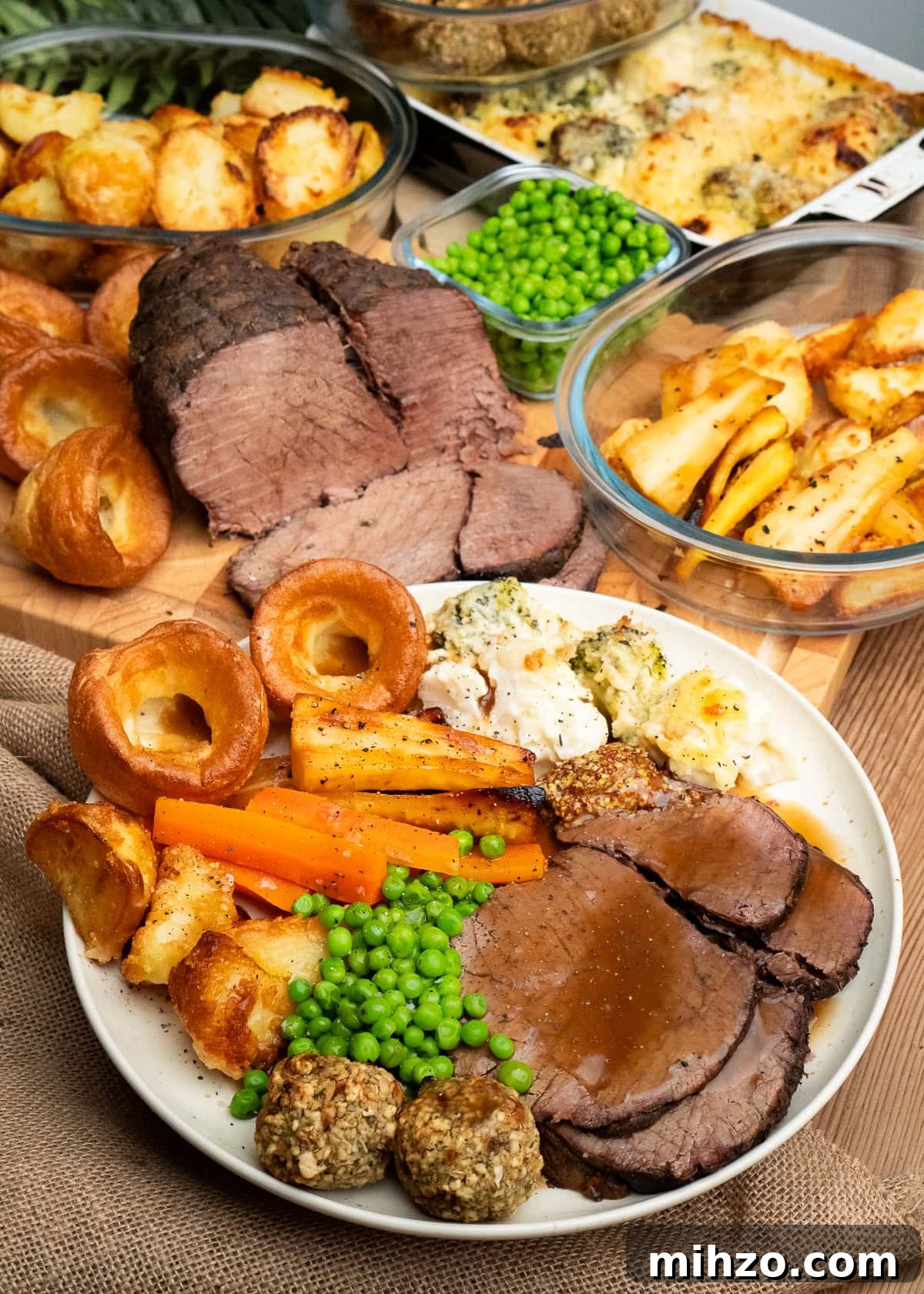Slow cooker roast beef dinner served with trimmings like cauliflower and broccoli cheese,Yorkshire puddings,parsnips, peas ,roast potatoes,carrots, stuffing balls and whole grain mustard