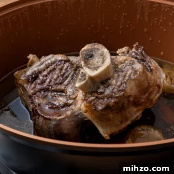 A cooked beef shin in a slow cooker on a vegetable trivet and gravy