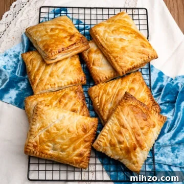 Eight cooked steak bakes stacked up on top of each other on a wire rack with a blue and white cloth under the wire rack