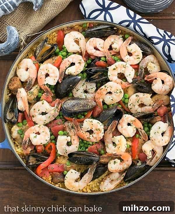 Julia Child's Paella a l'Americaine - Julia's twist on an extraordinary Spanish Classic with rice, saffron, shrimp, mussels and chorizo Overhead view of Paella a l'Americaine in a blue cast iron pan on a blue and white patterned napkin.