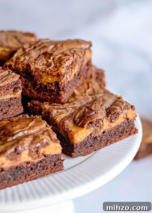 two pumpkin brownies in front of a white cake plate full of more brownies