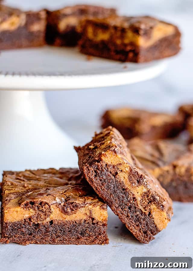 two pumpkin brownies in front of a white cake plate full of more brownies