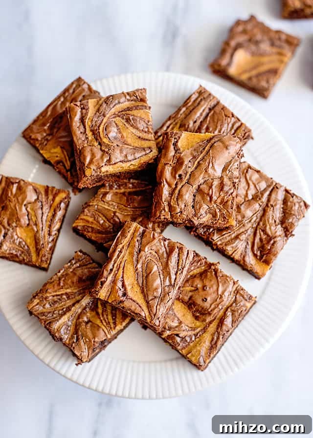 overhead view of pumpkin swirled brownies on a white cake plate and a marble background