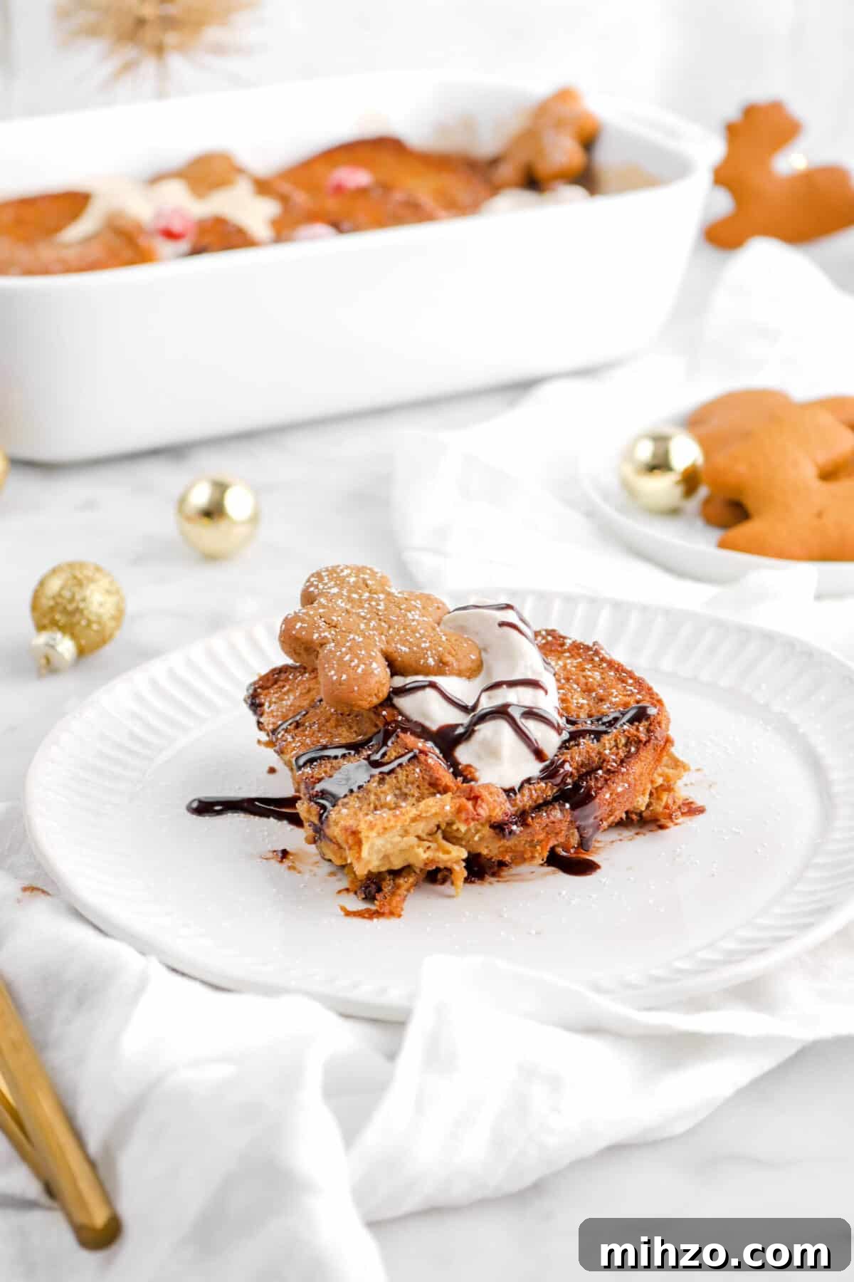 Overnight Gingerbread Chocolate Chip French Toast Bake 19 slice of gingerbread french toast on white plate with gold ornaments, cookies, and casserole behind
