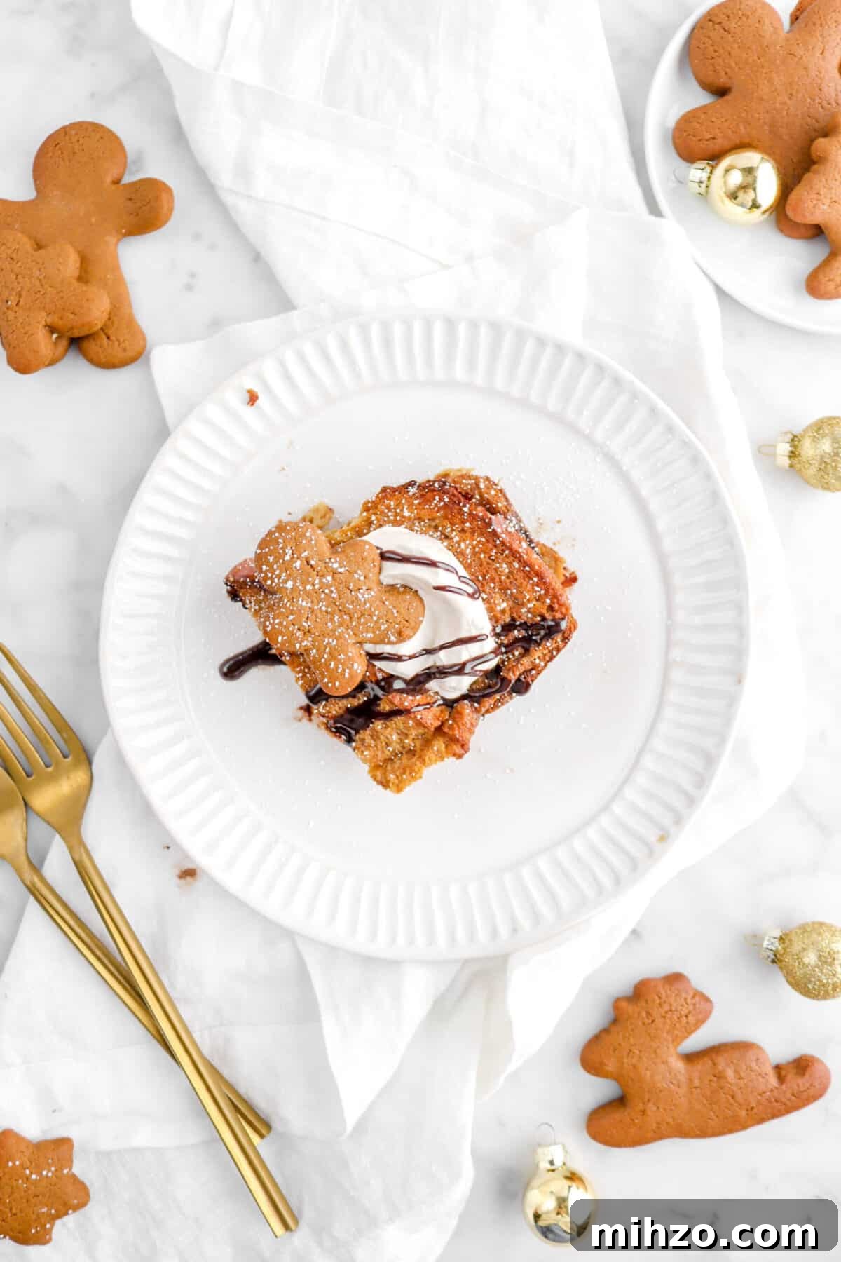 Overnight Gingerbread Chocolate Chip French Toast Bake 3 flat lay of slice of gingerbread french toast on white plate with cookies around, two forks, and gold ornaments