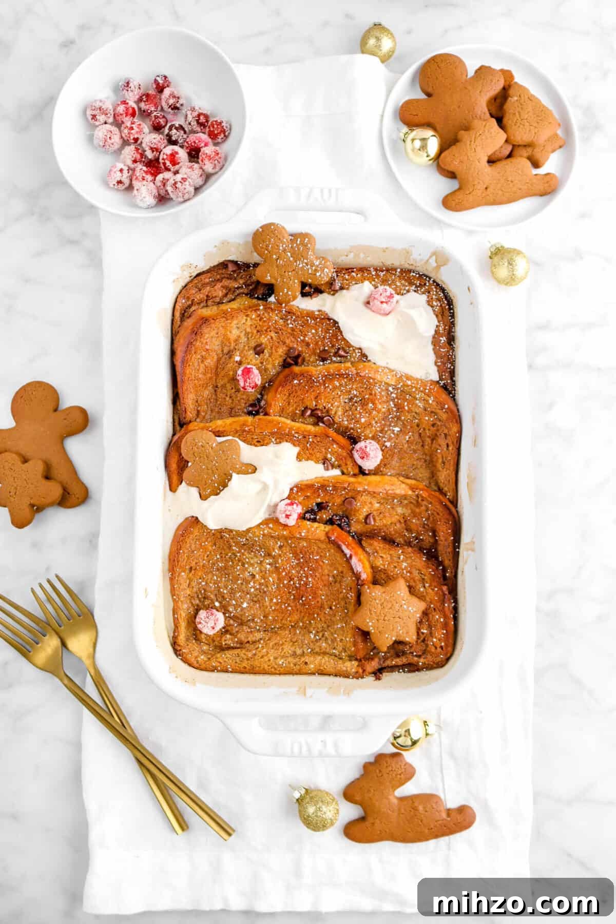 Overnight Gingerbread Chocolate Chip French Toast Bake 5 gingerbread french toast casserole on white napkin with whipped cream, sugared cranberries, and mini gingerbread men