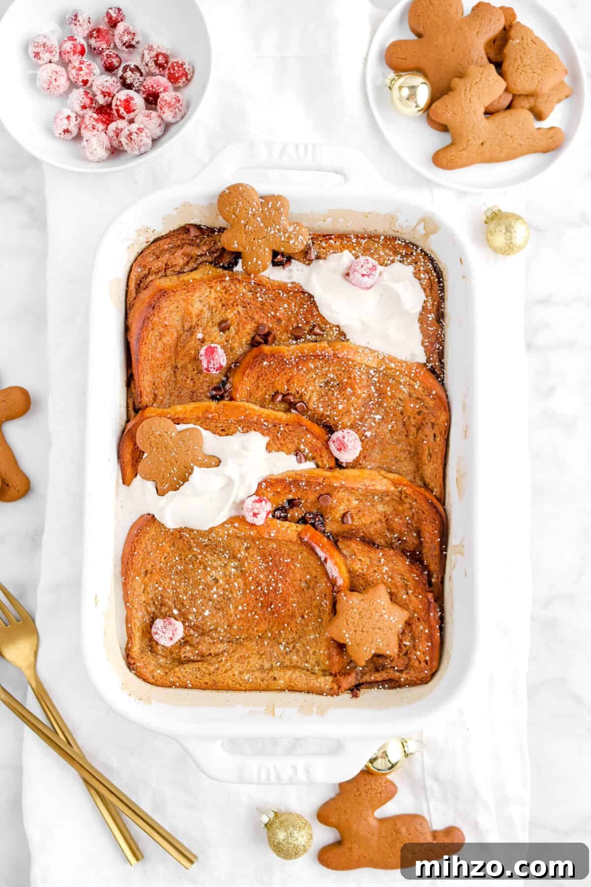 Overnight Gingerbread Chocolate Chip French Toast Bake 8 casserole on white napkin with gingerbread cookies, sugared cranberries, and mini gold ornaments
