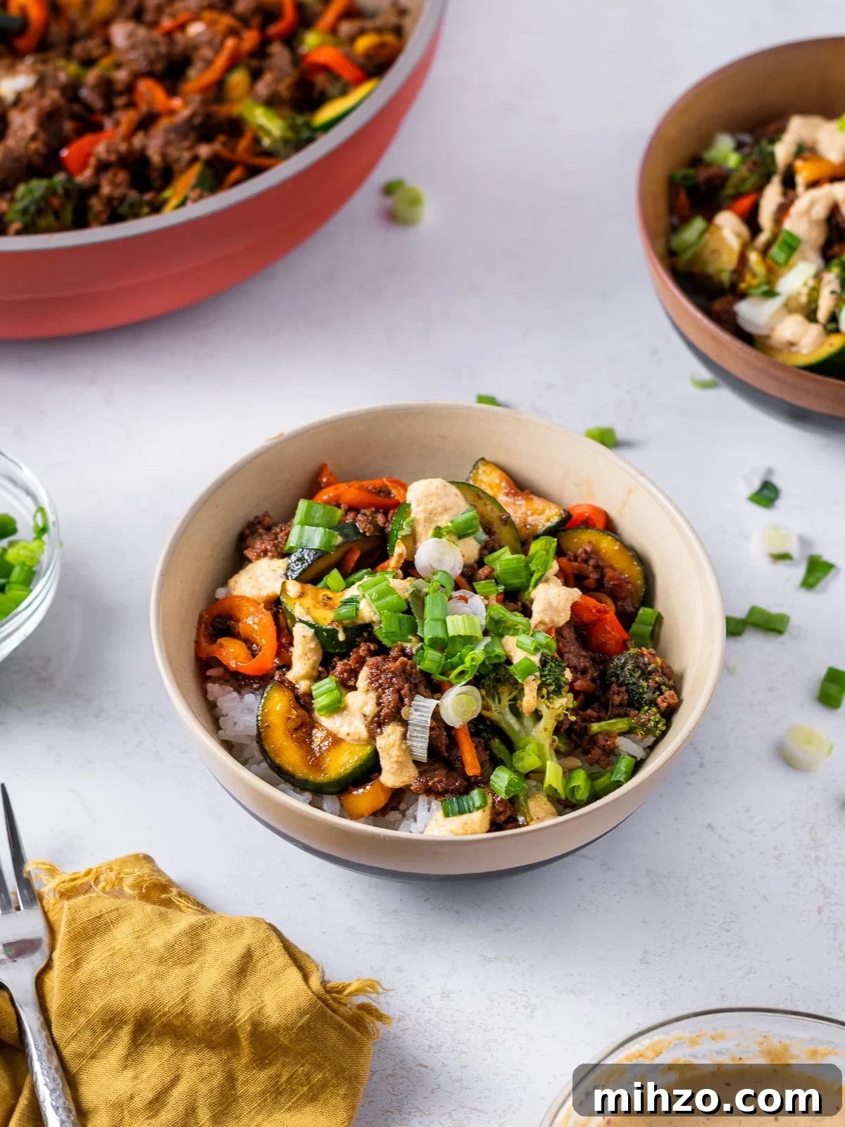 Teriyaki Beef Bowl with Spicy Kimchi Mayo Dressing 11 two bowls of teriyaki beef and vegetables, small bowl of green onions, skillet with extra teriyaki beef, bowl of kimchi mayo, napkin and fork