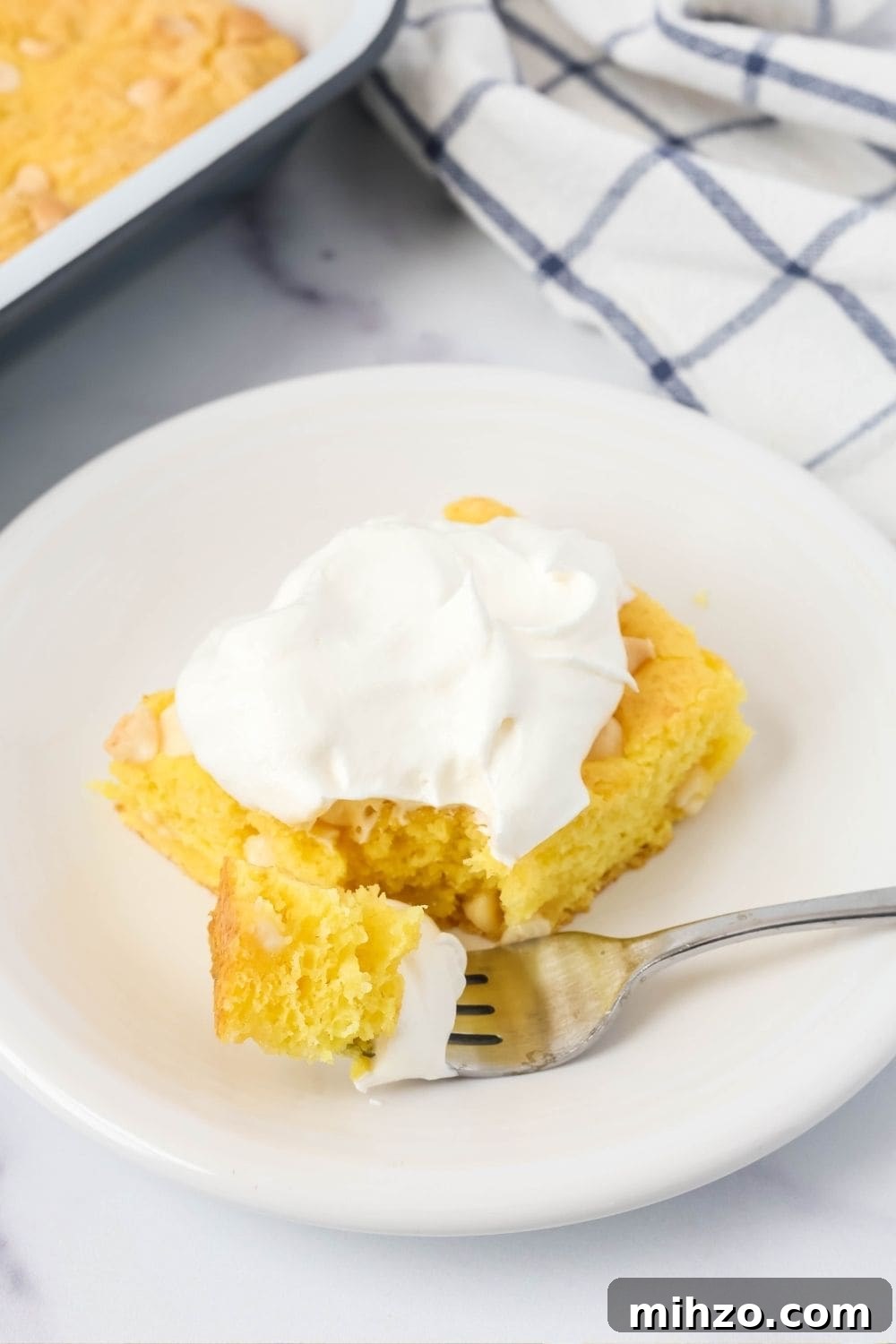 Creamy Lemon Pudding Dump Cake Recipe for Quick Desserts 8 slice of lemon dump cake, topped with whipped cream, on a dessert plate. A fork has removed a bite of the cake.
