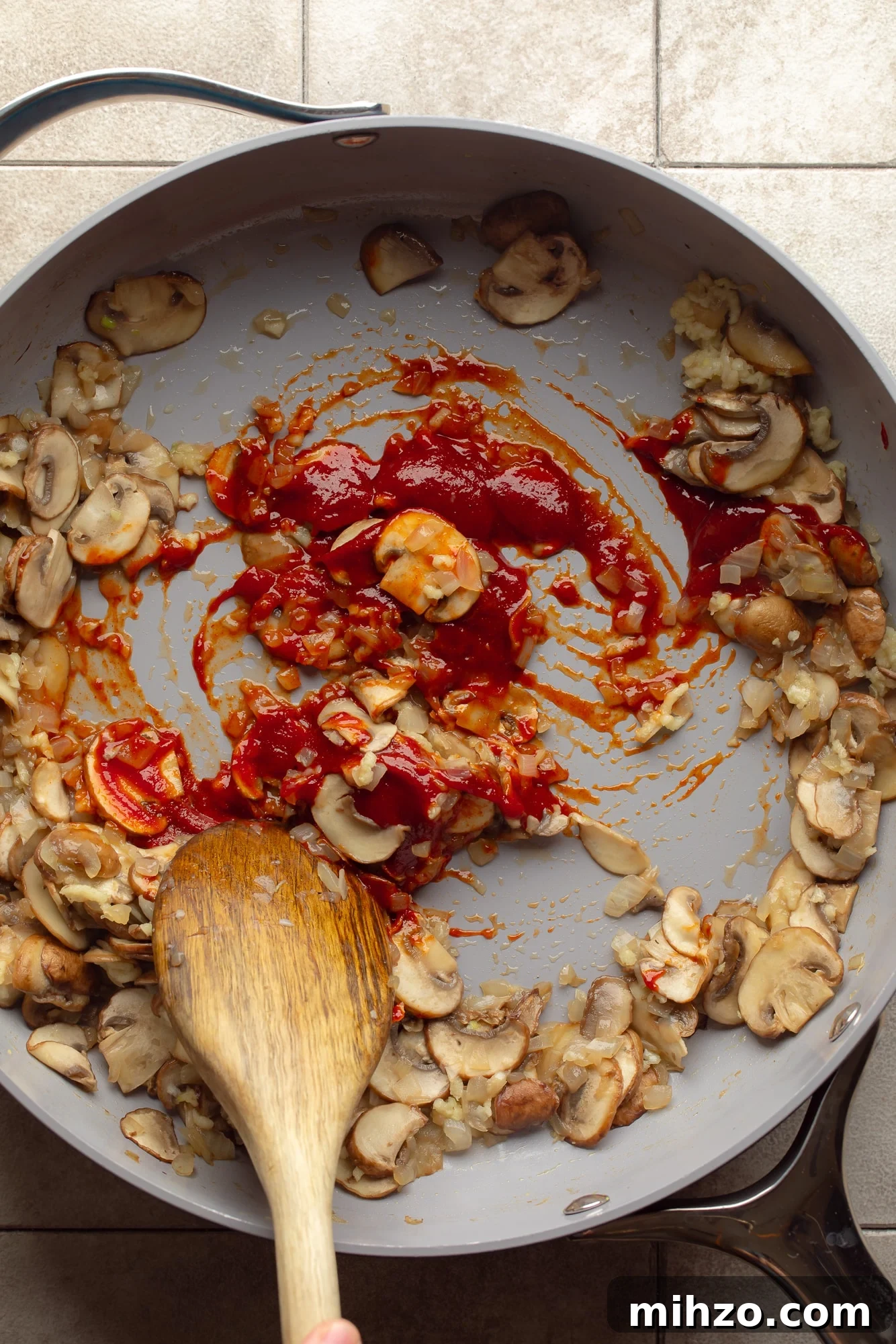 Creamy Gochujang Mushroom Noodles with Sesame and Scallions 3 overhead view of a wooden spoon stirring mushrooms and gochujang in a skillet.