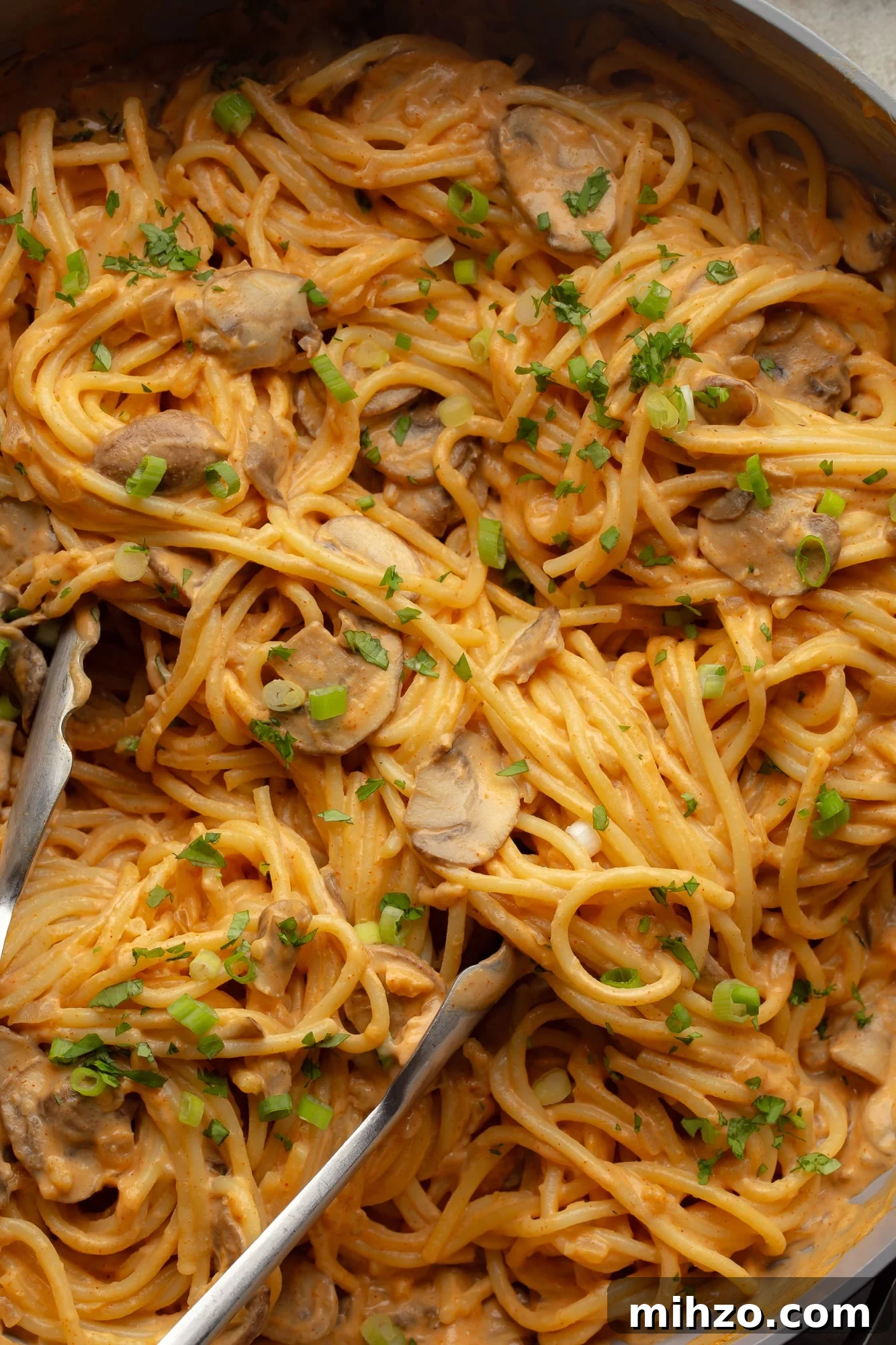 Creamy Gochujang Mushroom Noodles with Sesame and Scallions 8 close up on metal tongs in a batch of creamy gochujang noodles.