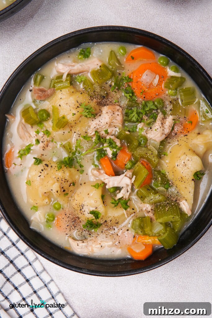 Gluten-Free Soup Dumplings Recipe: How to Make Juicy Xiao Long Bao 4 A black bowl filled with gluten-free dumplings, shredded chicken, carrots, celery, peas, and broth, topped with chopped parsley and black pepper.