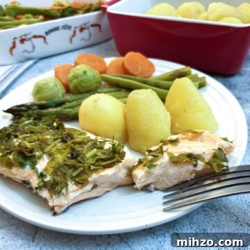 Lemon Herb Butter Salmon and Asparagus Parcels 6 A piece of salmon covered in dill and parsley on a plate with potatoes and vegetables.