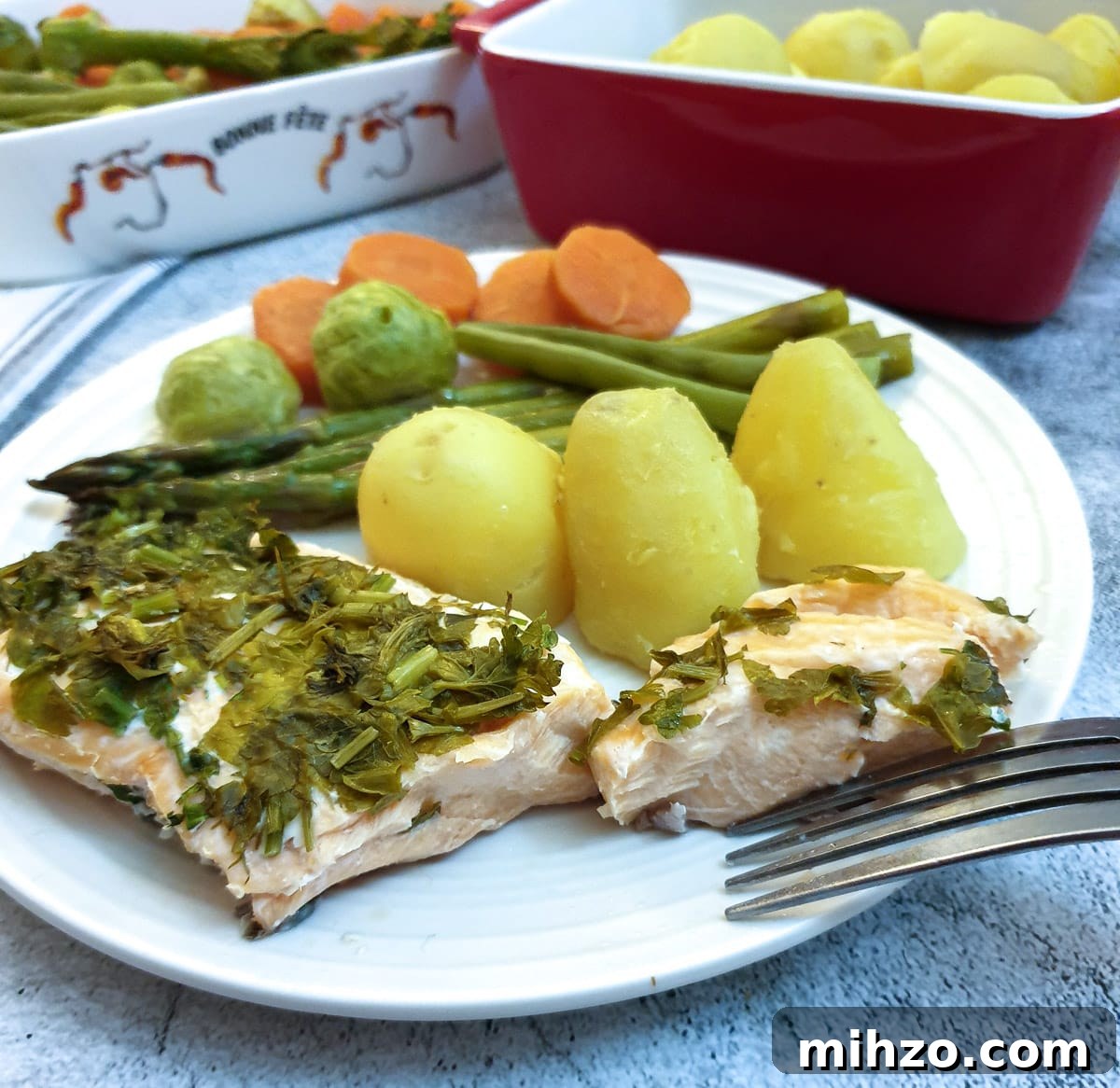 Lemon Herb Butter Salmon and Asparagus Parcels 7 A piece of salmon covered in dill and parsley on a plate with potatoes and vegetables.
