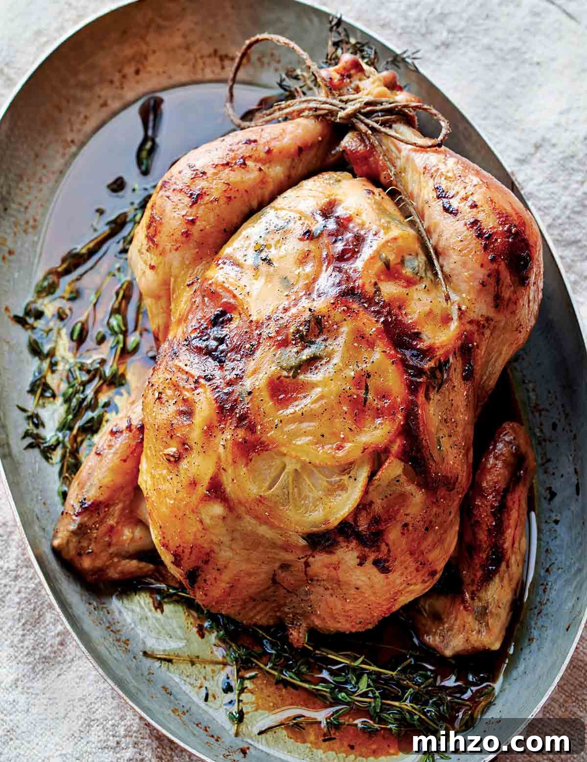8 Flavorful Whole Roast Chicken Recipes for Every Occasion 2 A whole roast chicken in an oval metal dish with fresh thyme scattered around it.