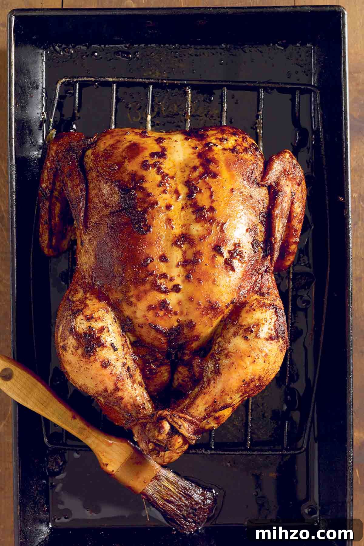 8 Flavorful Whole Roast Chicken Recipes for Every Occasion 8 A whole spicy roast chicken on a rack set inside a baking dish with a brush lying beside the chicken.
