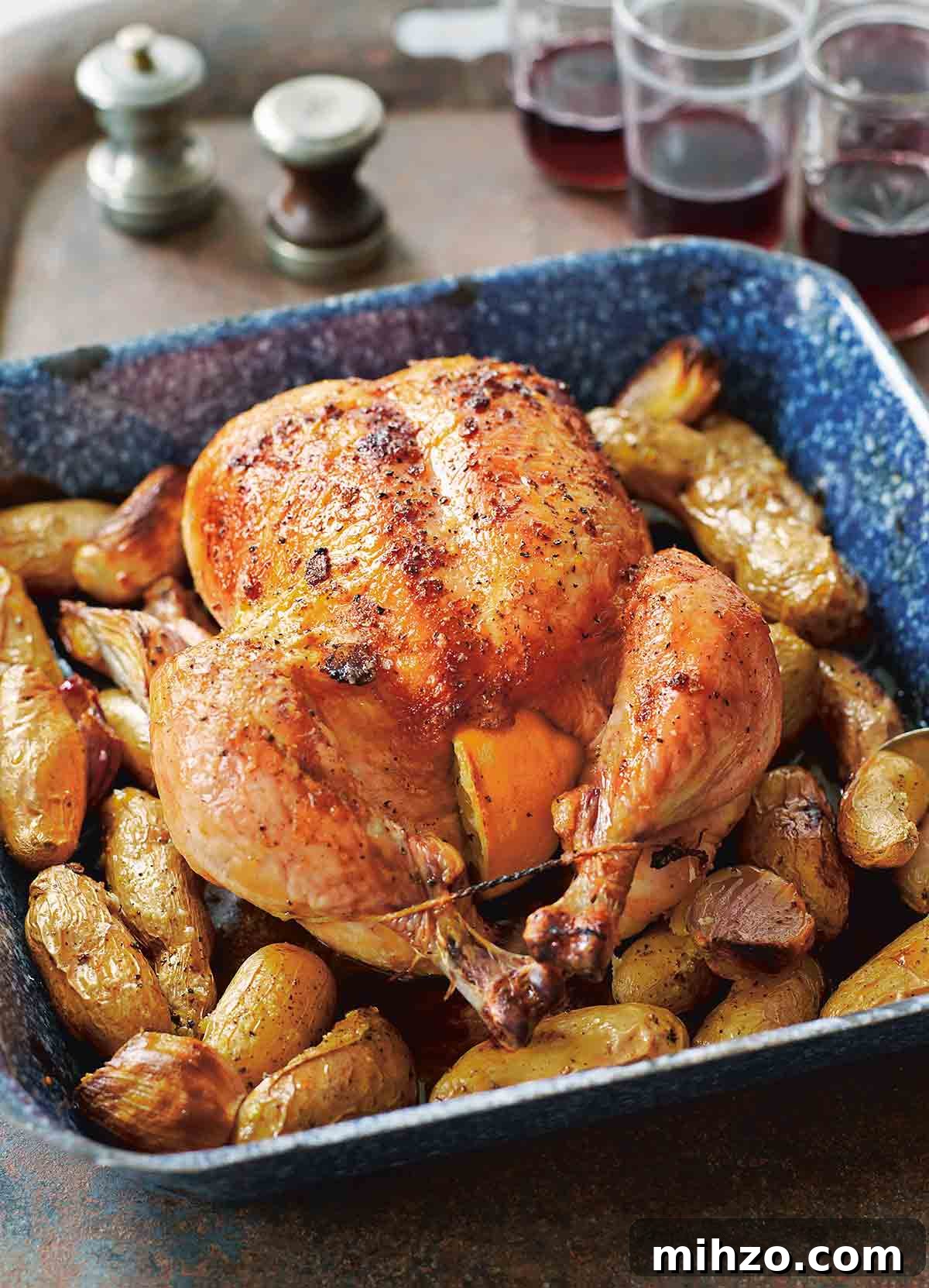 8 Flavorful Whole Roast Chicken Recipes for Every Occasion 10 A blue enamel roast pan with a maple roast chicken, trussed and stuffed with lemon halves, sitting on a bed of fingerling potatoes.