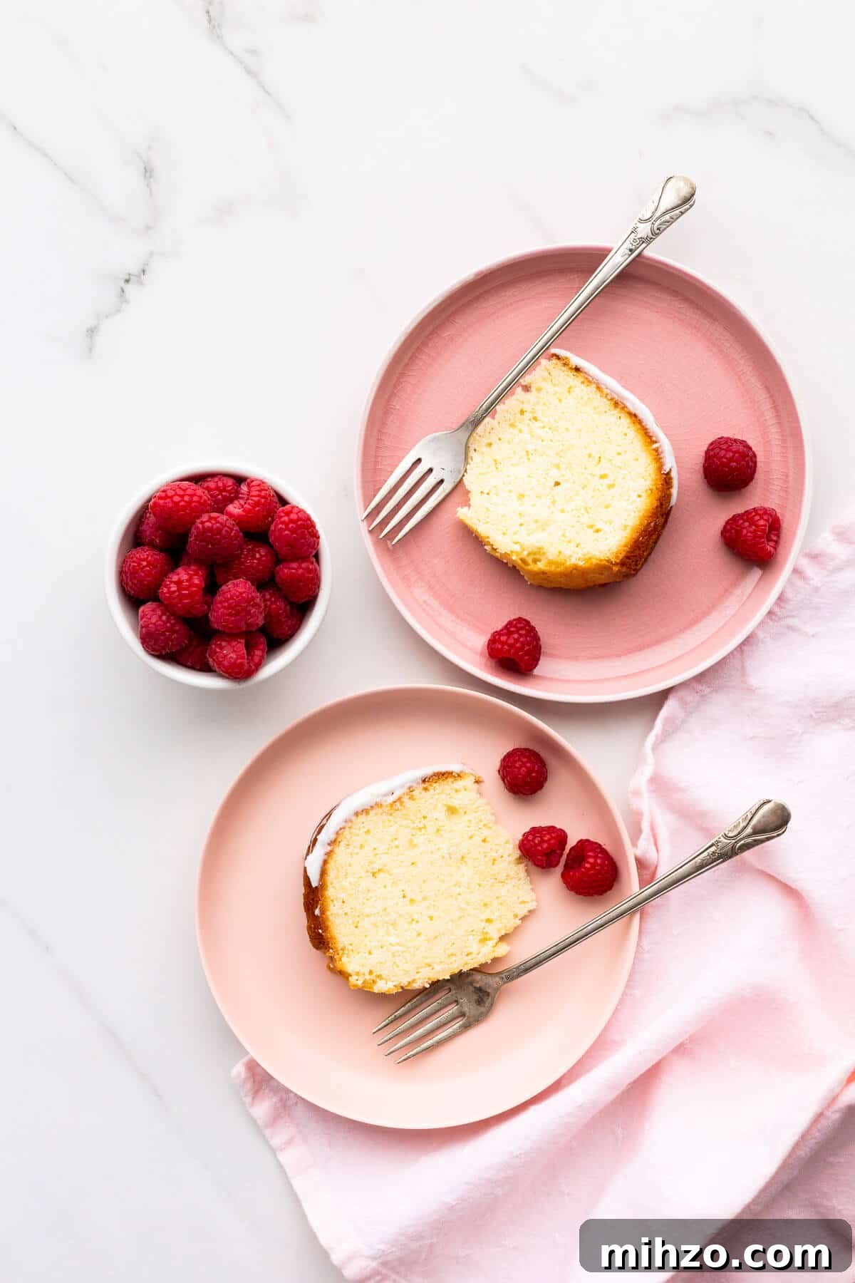 Moist Lemon Loaf Cake Recipe with Zesty Glaze 2 Slices of lemon cake on pink plates, served with raspberries.
