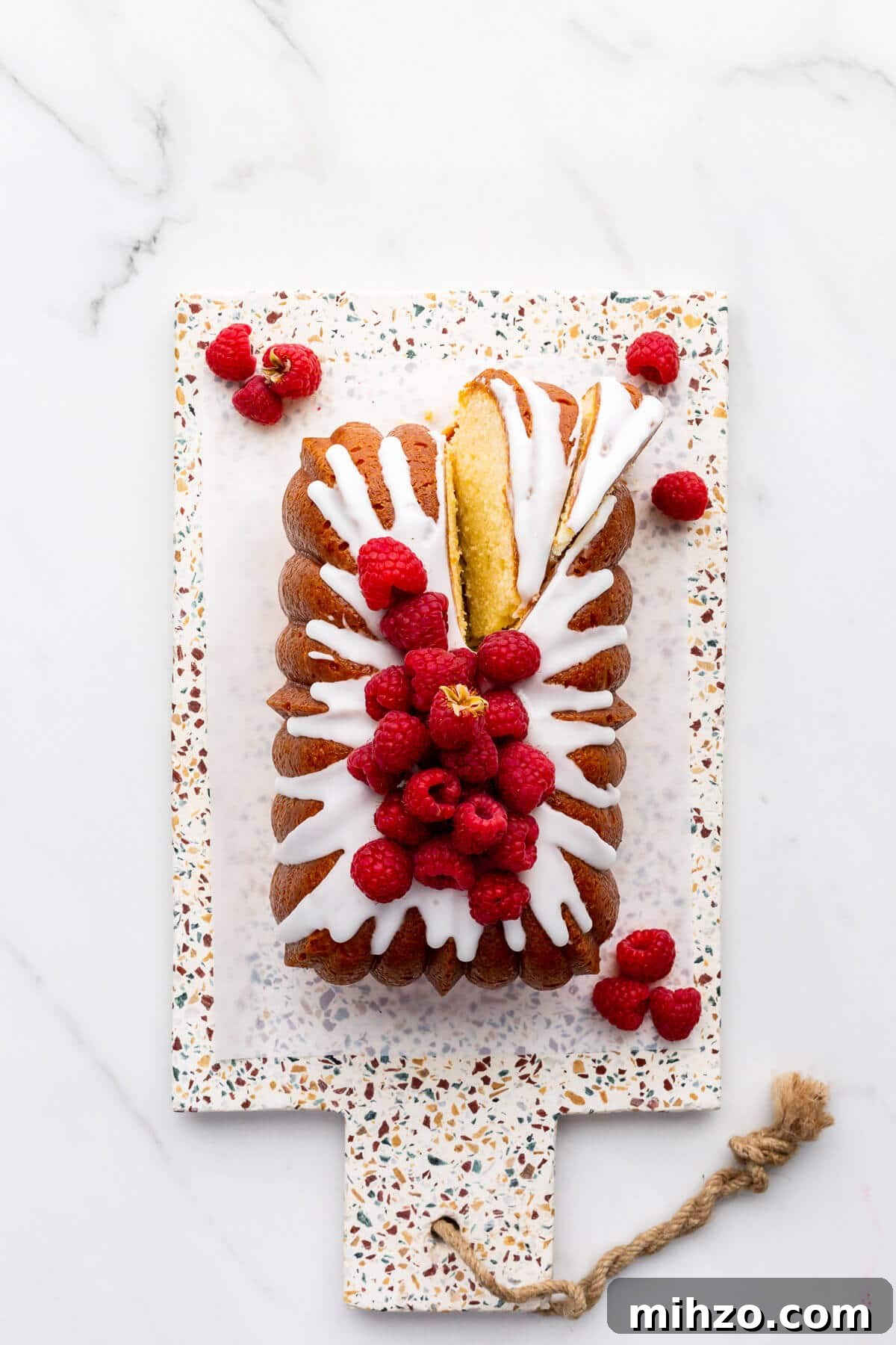Moist Lemon Loaf Cake Recipe with Zesty Glaze 11 Lemon loaf cake topped with lemon icing and fresh raspberries being sliced to serve it