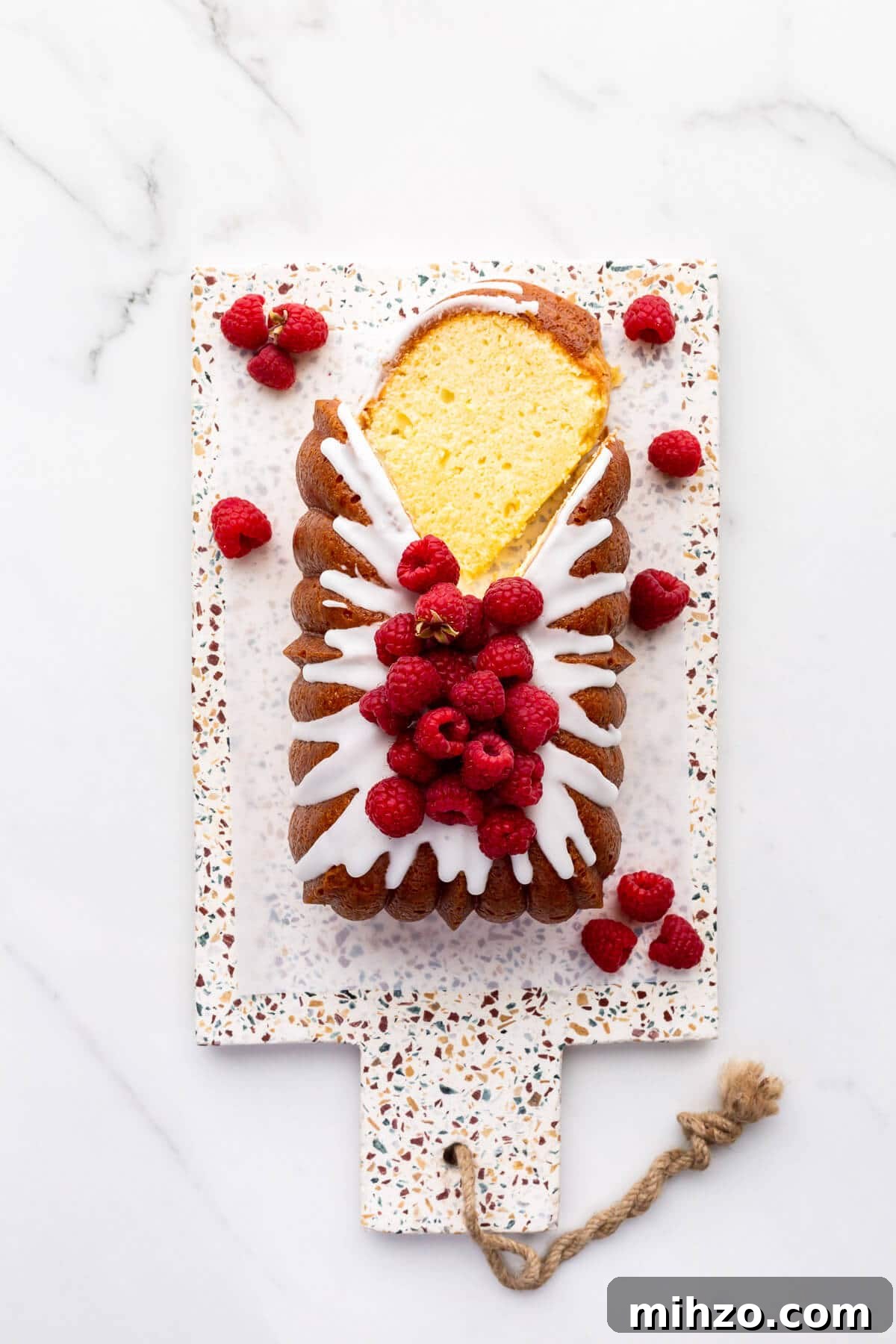 Moist Lemon Loaf Cake Recipe with Zesty Glaze 12 Iced lemon loaf cake on a terrazzo board being sliced.