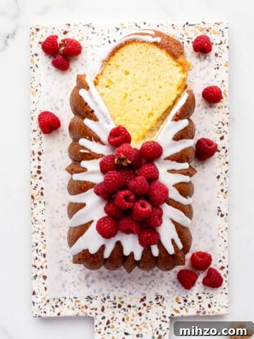 Lemon loaf cake topped with lemon icing and fresh raspberries being sliced to serve it