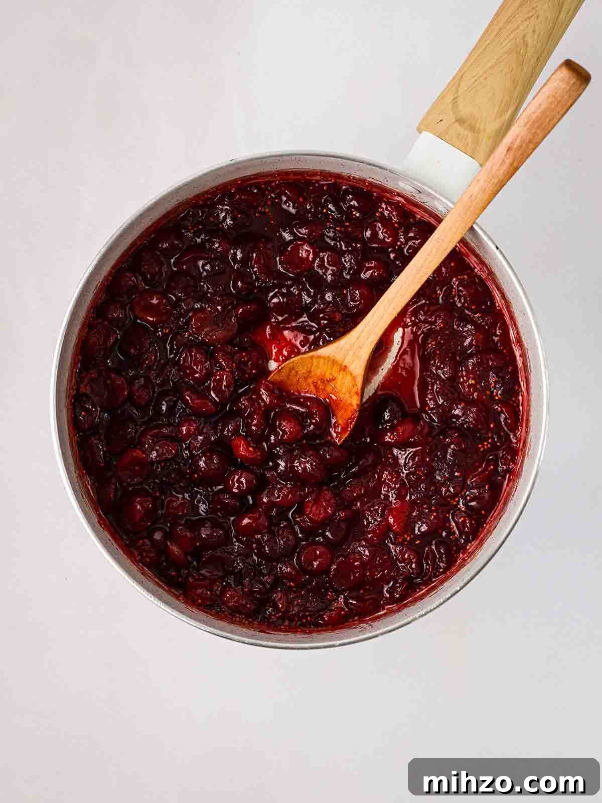 Cranberry sauce in a pan with a wooden spoon, stirring.