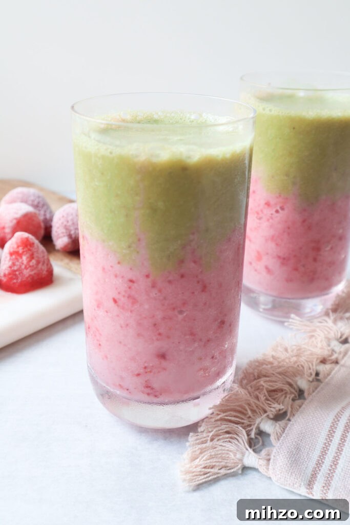 two glasses with strawberry matcha smoothie with a pink strawberry layer at the bottom and a green matcha layer on top