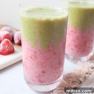 two glasses with strawberry matcha smoothie with a pink strawberry layer at the bottom and a green matcha layer on top