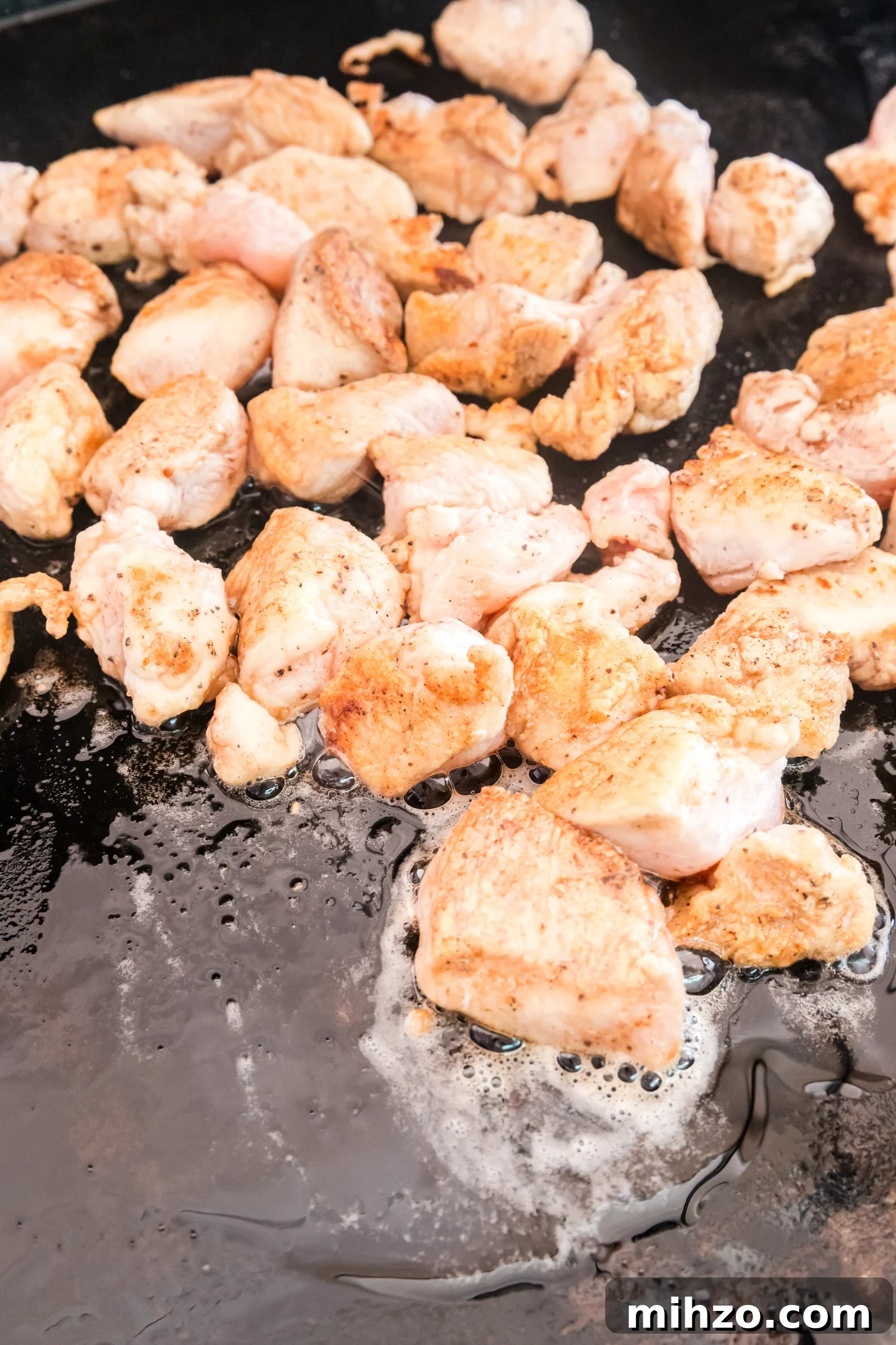 Bite-sized chicken pieces cook on a flat-top griddle