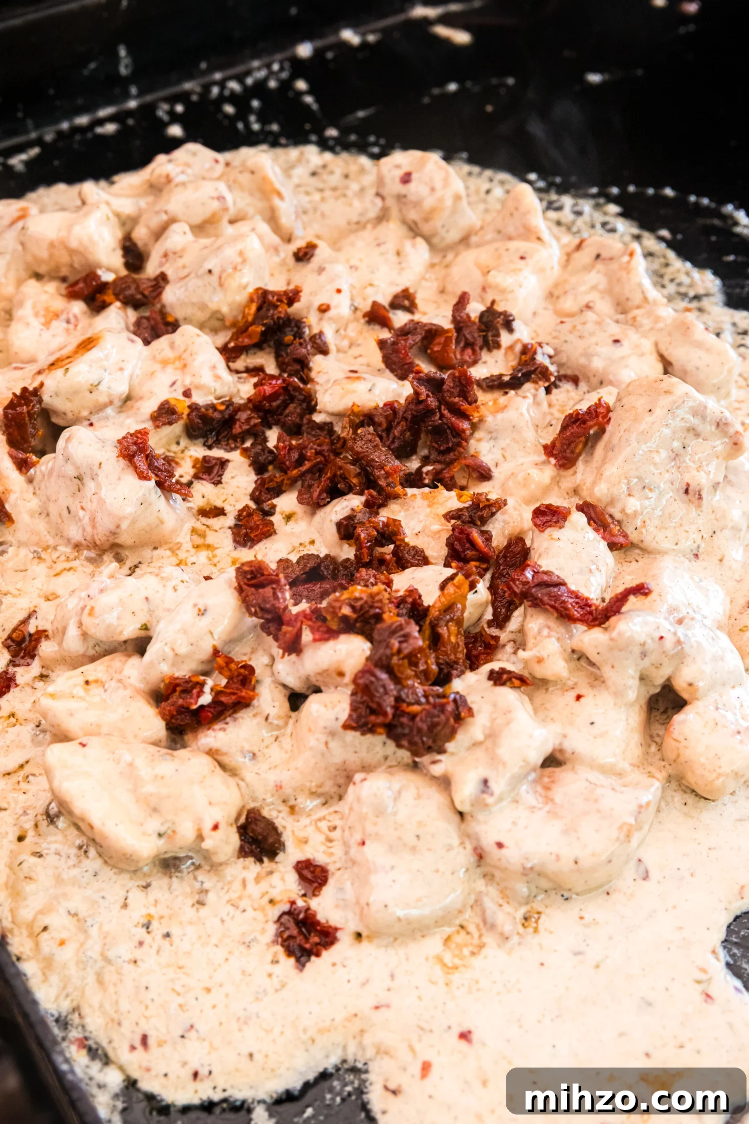 Chicken simmers in a creamy sauce on the griddle, topped with chopped sun-dried tomatoes as the sauce thickens and bubbles.